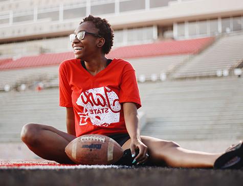 一名身着Jax State t恤的JSU女学生坐在JSU体育场的球场上，面前放着一个足球